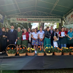 Organizatorzy, uczestnicy i laureaci 1 Etapu Bitwy Regionów w Kościerzynie pozują wspólnie  do pamiątkowego zdjęcia na scenie na której stoją kosze z kwiatami