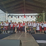 Grupa osób ubranych na ludowo pozują wspólnie na scenie do pamiątkowego zdjęcia